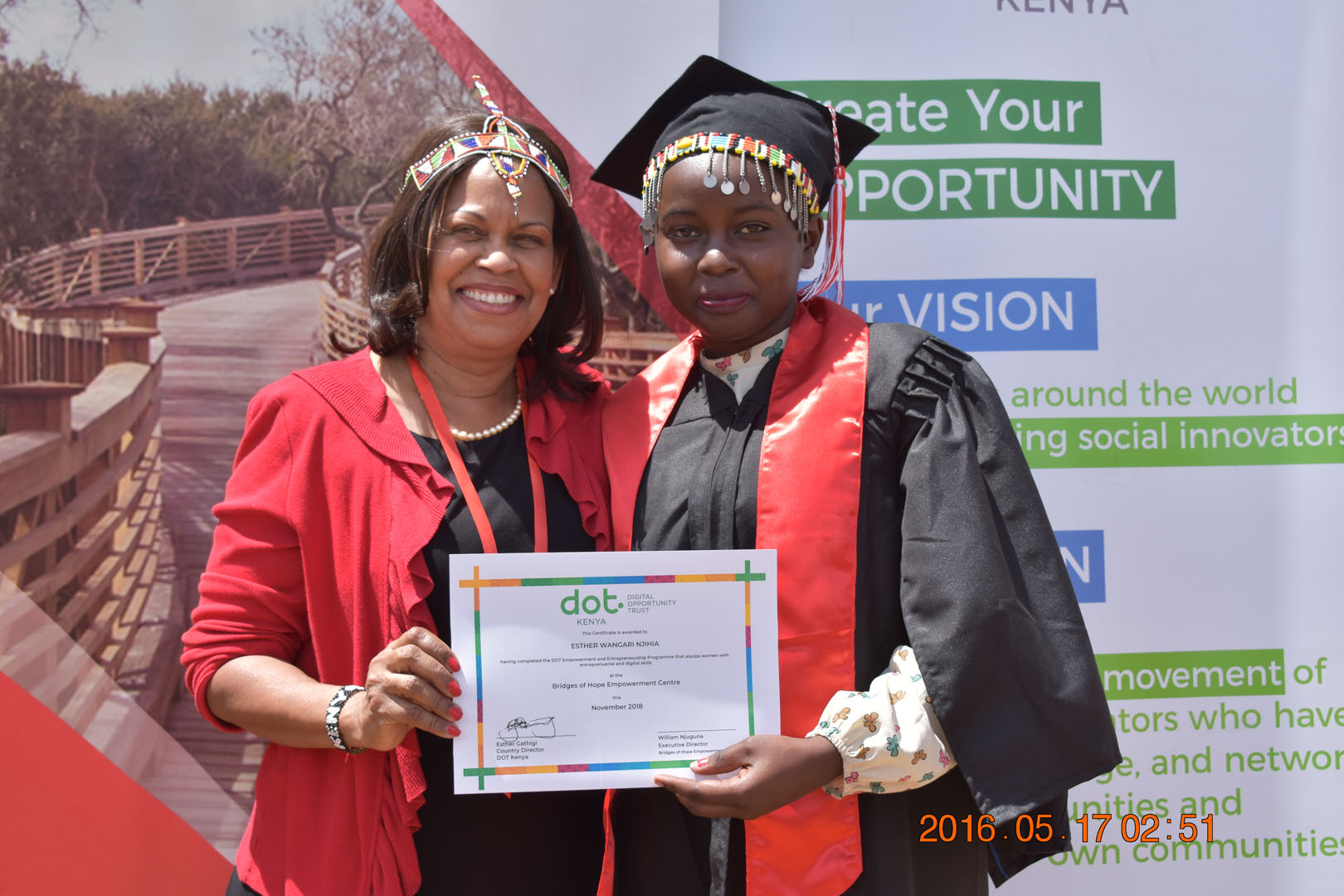 Two women in graduation attire holding a certificate.