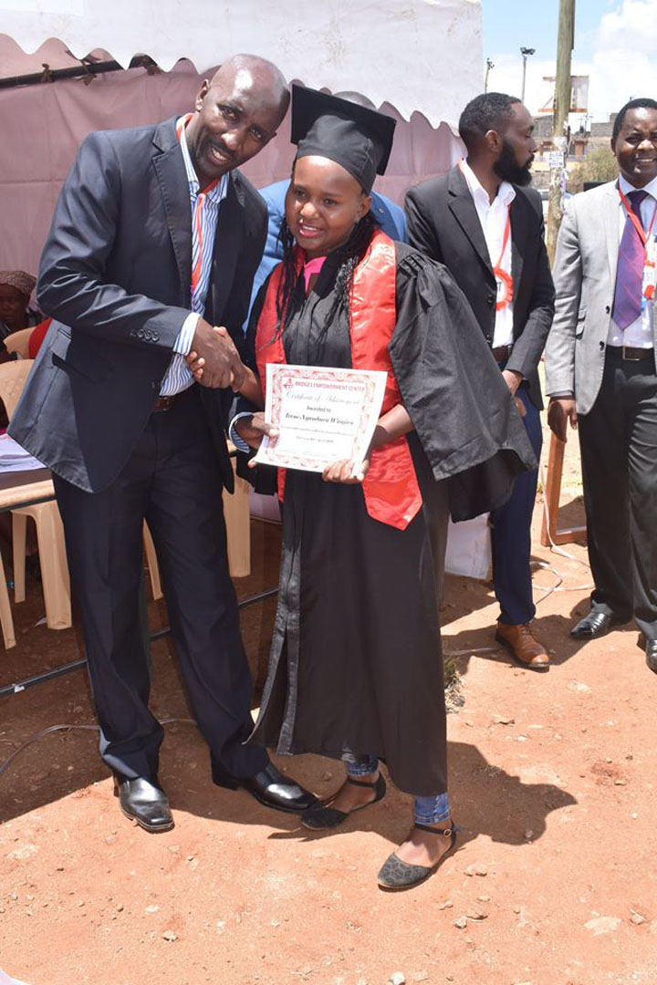 A woman in graduation gown shaking hands with a man.