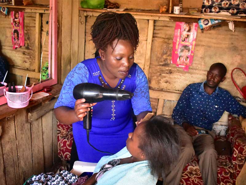 A woman blow drying another person 's hair.