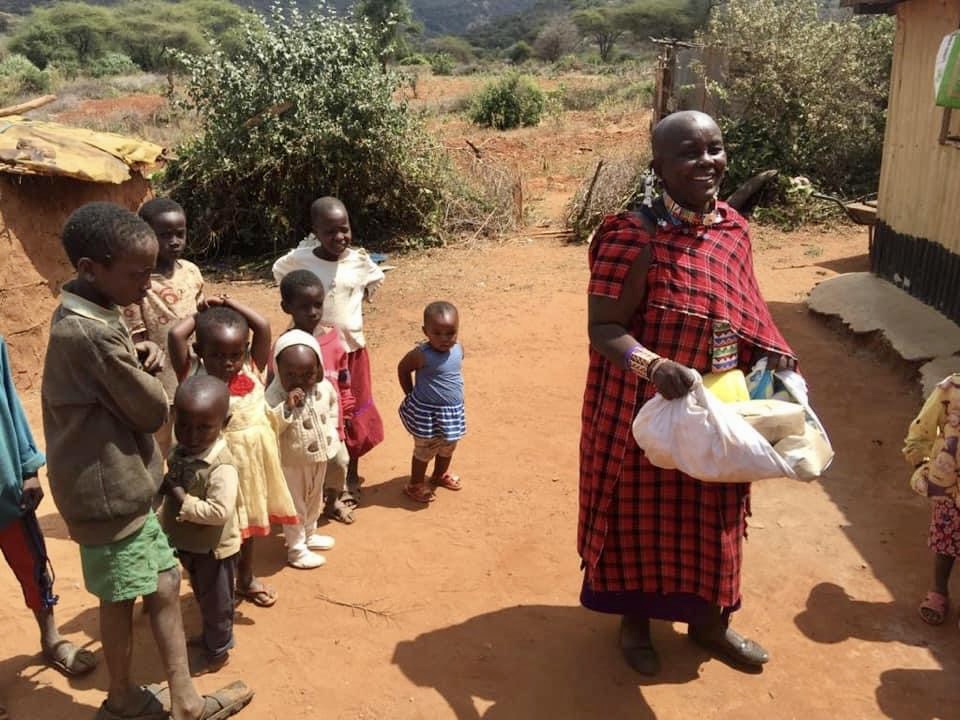 A woman holding a bag of food in front of a group of children.